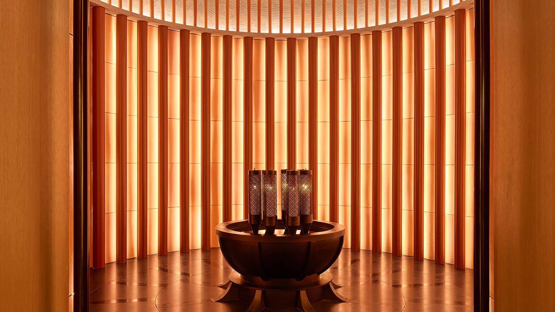 Interior of the spa entrance with lit cylindrical lamps on a central table at The RuMa Hotel and Residences